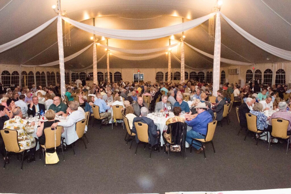 members sitting at tables inside outdoor tent